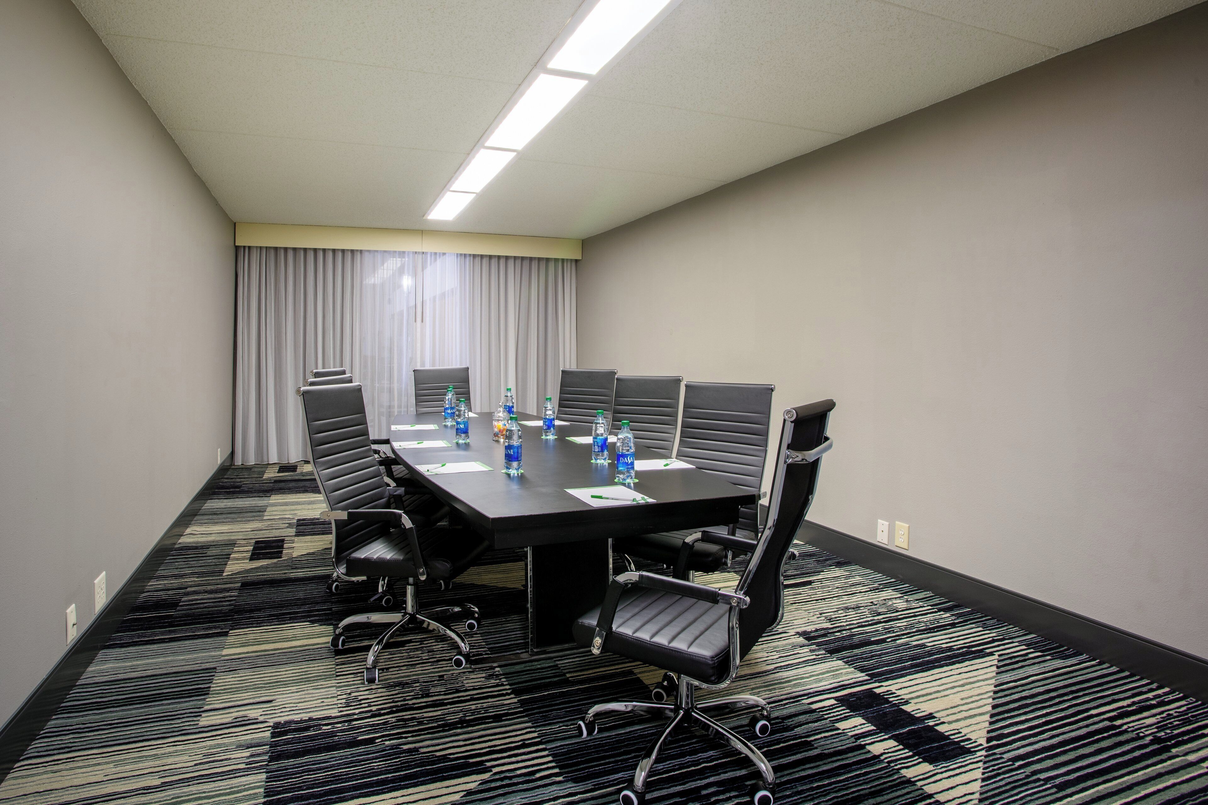Una sala de conferencias con una mesa rectangular, seis sillas y botellas de agua sobre la mesa.