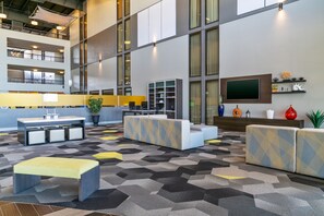 A spacious lobby with a high ceiling, multiple seating areas, a reception desk, and a large TV screen. - Holiday Inn Morgantown - Reading Area by IHG (Morgantown)