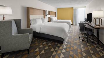 A hotel room with two beds, a desk, a chair, and a patterned carpet.