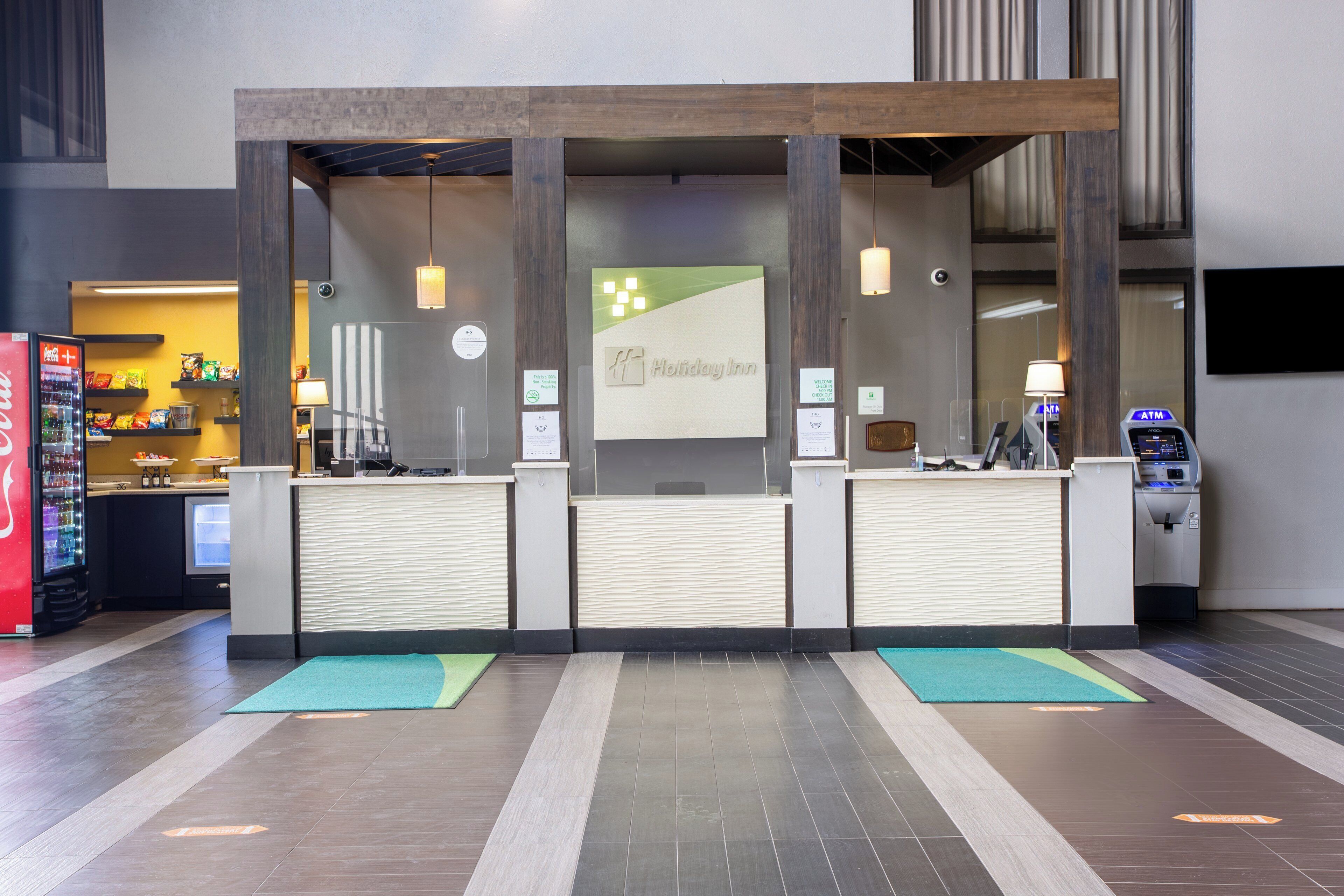 A reception desk with a Holiday Inn sign, a Coca-Cola refrigerator, and an ATM.