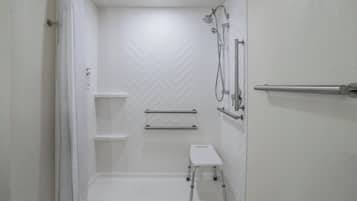 A white bathroom with a chevron-patterned wall, a shower with a handheld showerhead, a grab bar, a small step stool, and a towel rack.