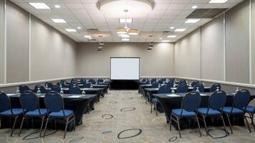 A conference room with rows of tables and chairs, a projector screen, and a patterned carpet.