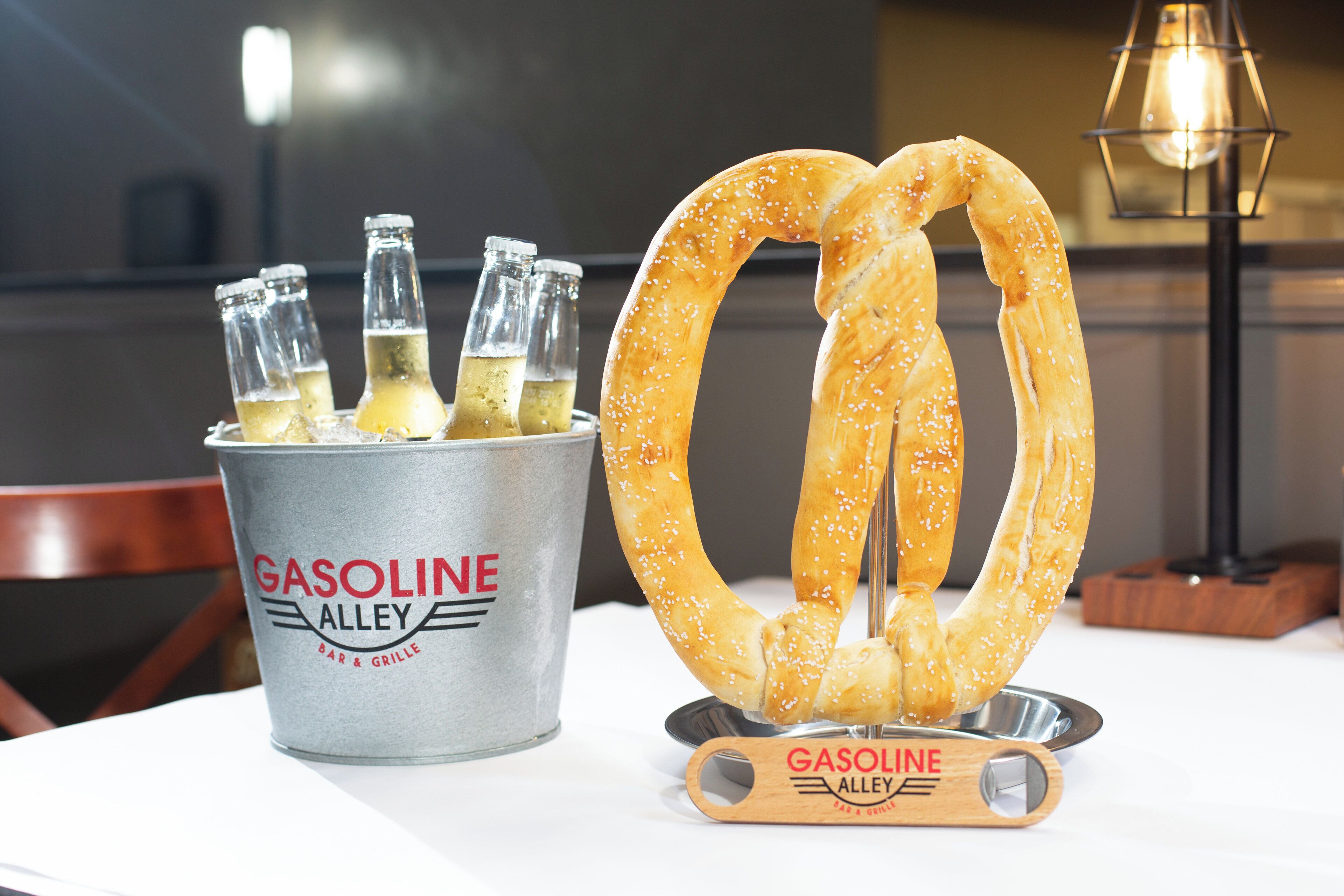 Un cubo etiquetado 'GASOLINE ALLEY' con botellas y un pretzel sobre una mesa.