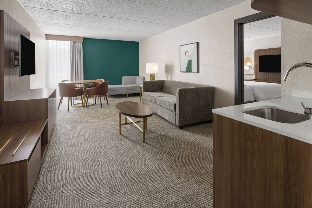 A hotel room with a seating area, a sofa, a TV, a desk, and a bathroom.