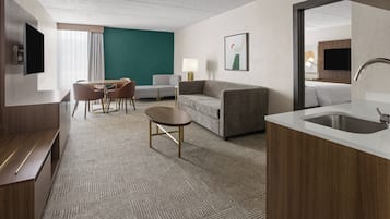 A hotel room with a seating area, a sofa, a TV, a desk, and a bathroom.