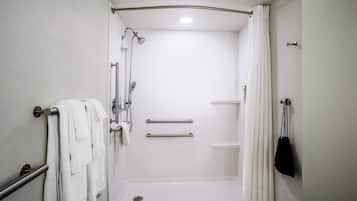A wheelchair-accessible shower stall with grab bars, a white tiled floor, and a white curtain.