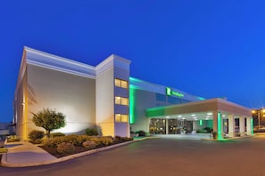 A Holiday Inn hotel with a modern design, featuring a well-lit entrance and a landscaped area with bushes and a tree. - Holiday Inn Morgantown - Reading Area by IHG (Morgantown)