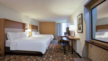 Habitación de hotel con dos camas, un escritorio, una silla, un espejo grande y una alfombra estampada.