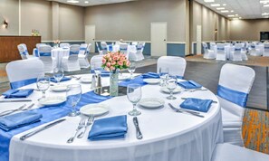 A banquet hall with round tables set for dining, white chairs with blue sashes, and a central floral arrangement. - Holiday Inn Morgantown - Reading Area by IHG (Morgantown)