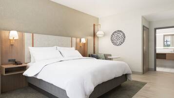 A modern hotel room with a large bed, bedside tables with lamps, a round wall decoration, and a view of the bathroom.
