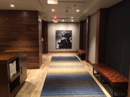 A hallway with wooden flooring, a blue striped carpet, a bench, and a wall-mounted poster.