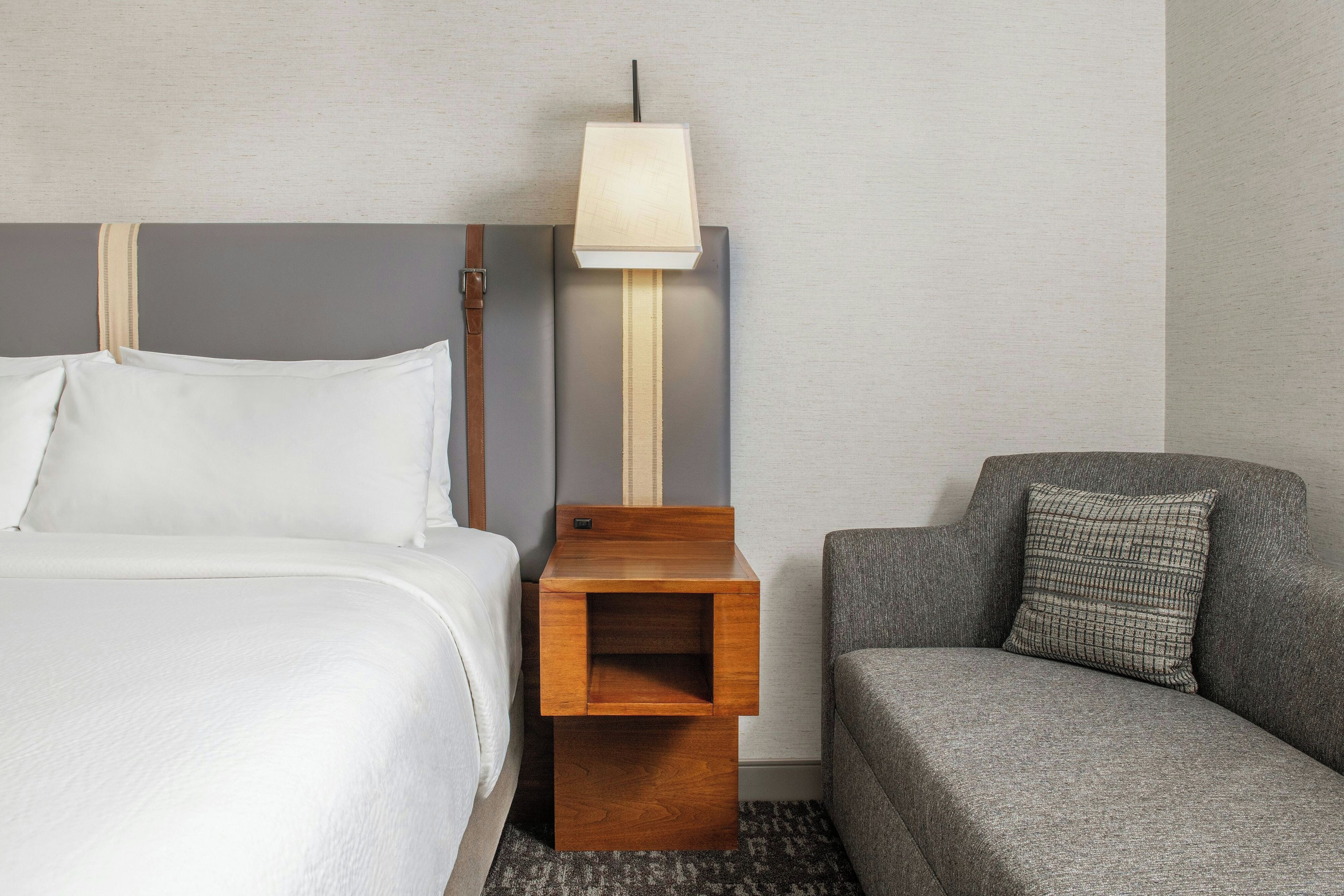 A hotel room with a bed, a nightstand, a lamp, a sofa, and a wall with a textured pattern.