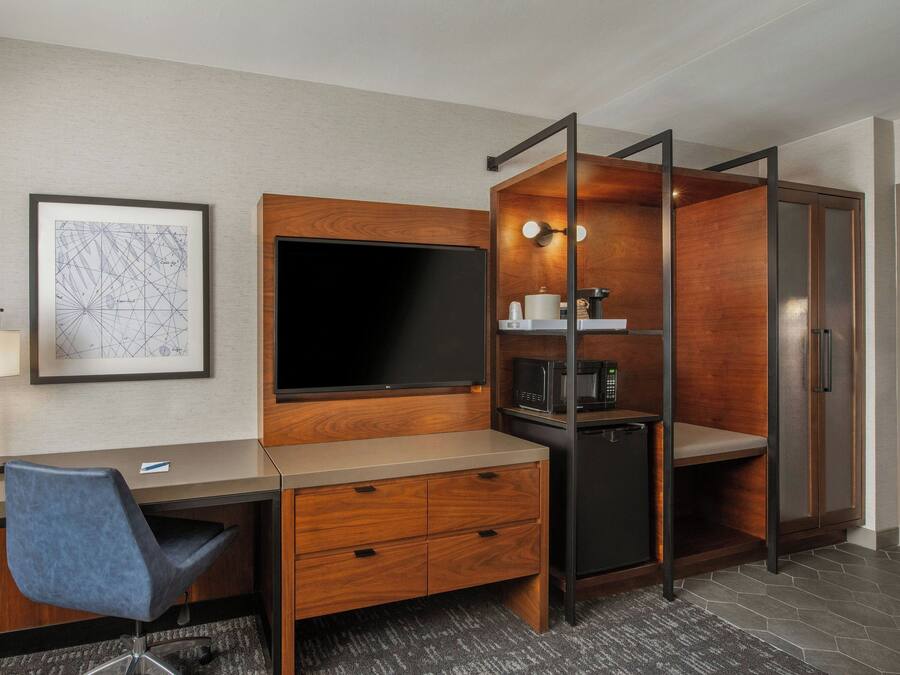 A hotel room with a desk, chair, TV, minibar, and a door with a lock.