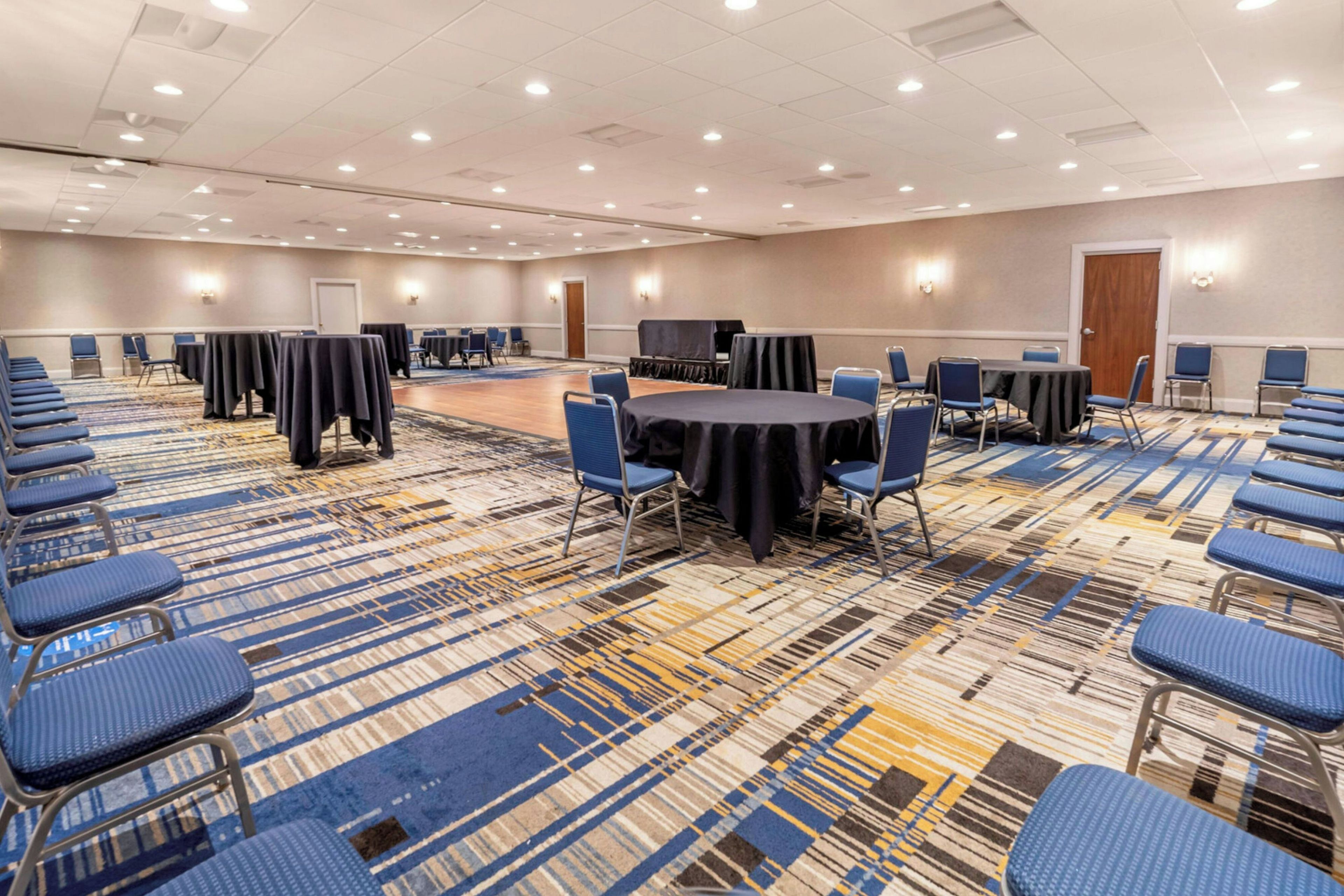 A conference room with multiple tables and chairs, carpeted flooring, and recessed lighting.