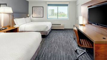 Een hotelkamer met twee bedden, een bureau, een flatscreen televisie, een raam met uitzicht op de stad en een kunstwerk in een lijst aan de muur.