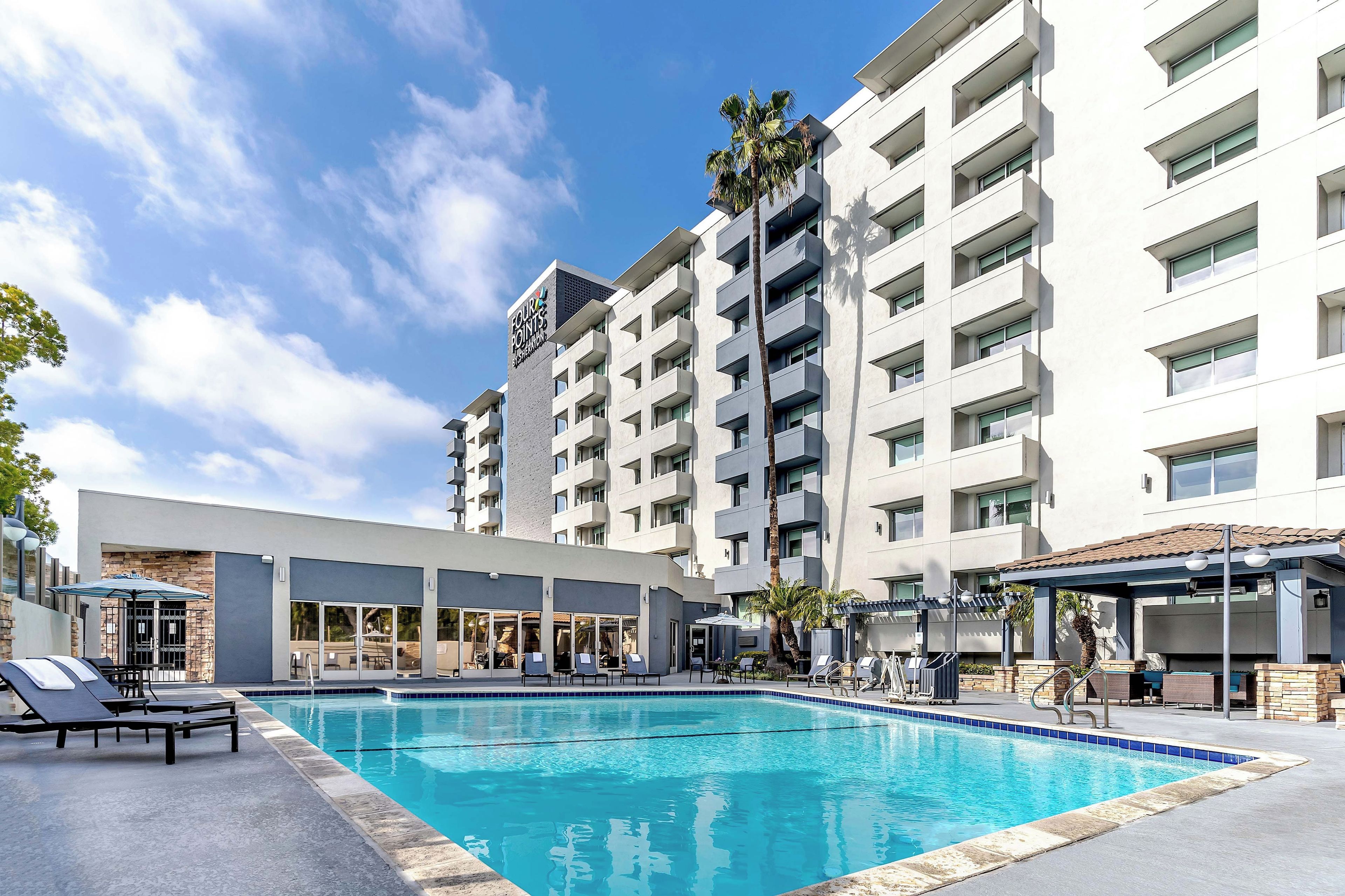 A hotel with a swimming pool, outdoor seating, and a multi-story building.