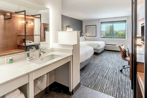 Habitación de hotel moderna con un espejo grande, un lavamanos, una cama, una silla y una ventana con vista a la ciudad.
