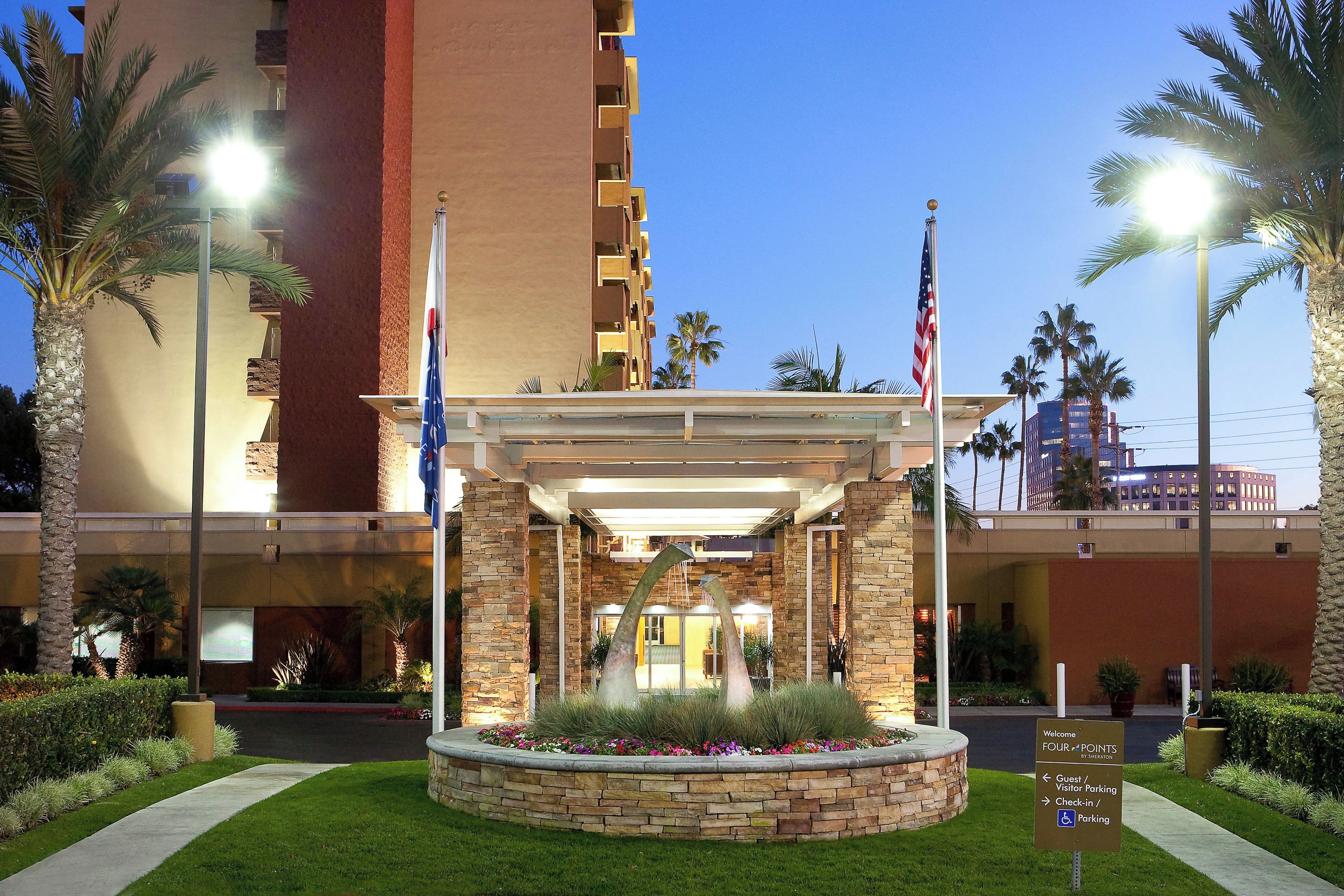 A hotel entrance with a stone facade, palm trees, and an American flag.