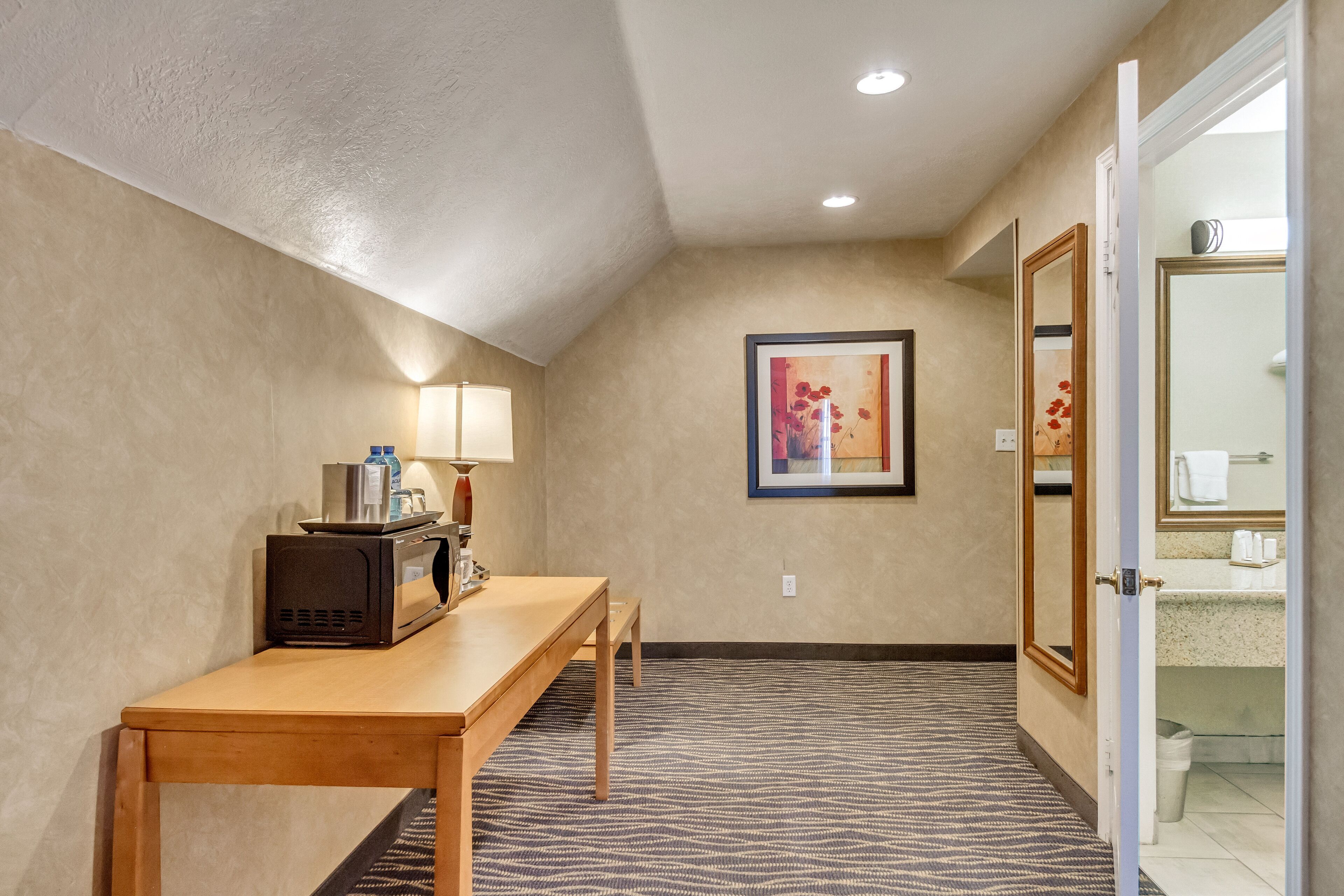 A hotel hallway with a wooden table, a microwave, a lamp, and a framed picture on the wall.