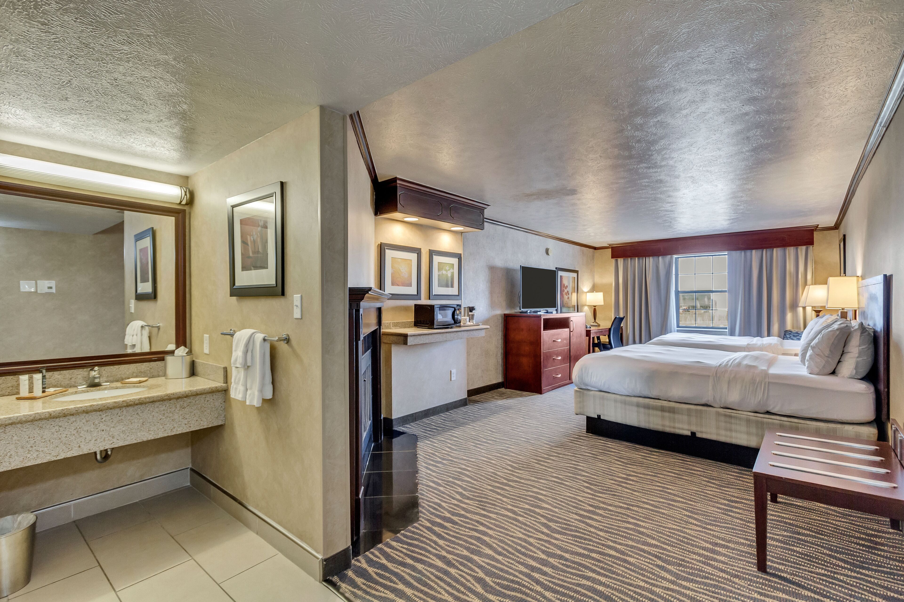 Une chambre d’hôtel dotée d’un grand lit, d’une salle de bain séparée avec un meuble-lavabo, d’une kitchenette et d’un téléviseur à écran plat.