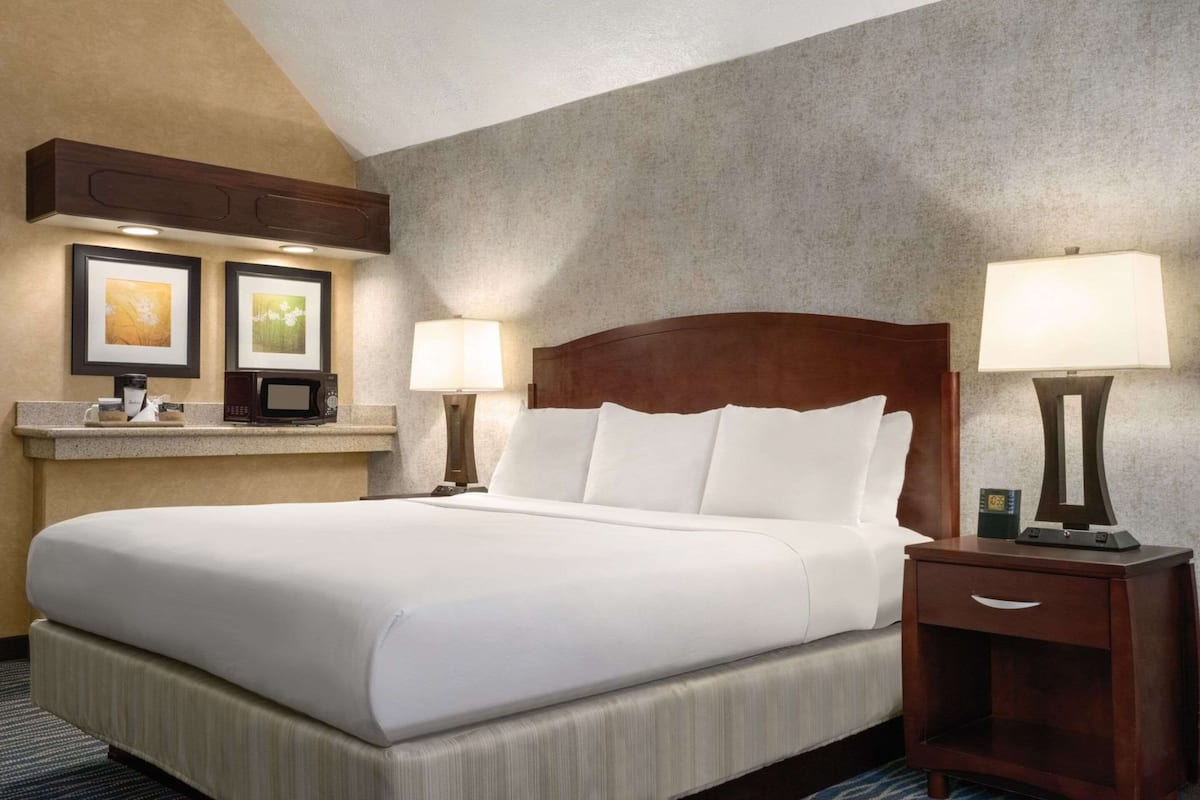 A hotel room with a large bed, two bedside tables with lamps, a small desk with a lamp, and framed artwork on the wall.
