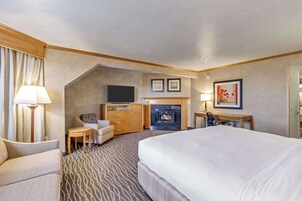 Habitación de hotel con una cama grande, televisor, chimenea, escritorio y una silla.