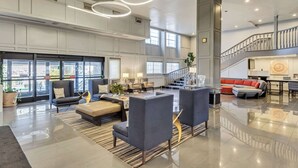 Eine geräumige Lobby mit hoher Decke, großen Fenstern und einer Treppe, die zu einer oberen Ebene führt.