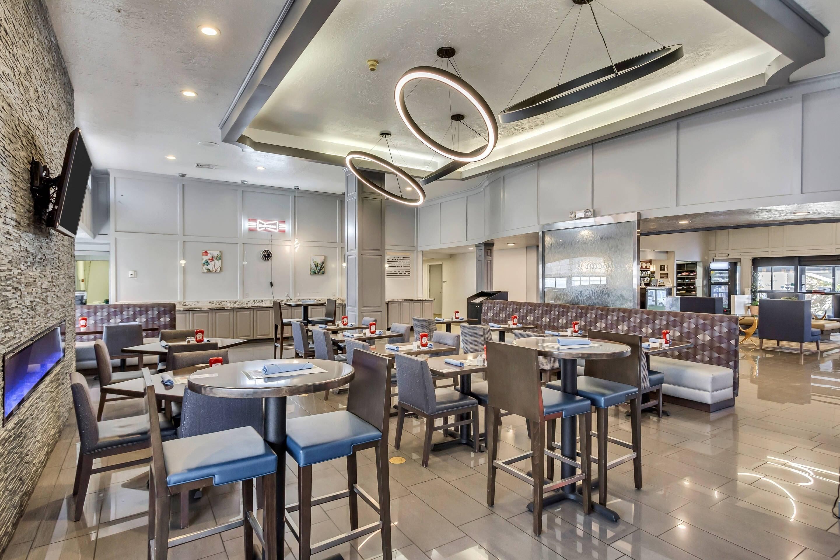 Un restaurante moderno con mesas redondas, asientos de bar y una pared decorada con piedra.