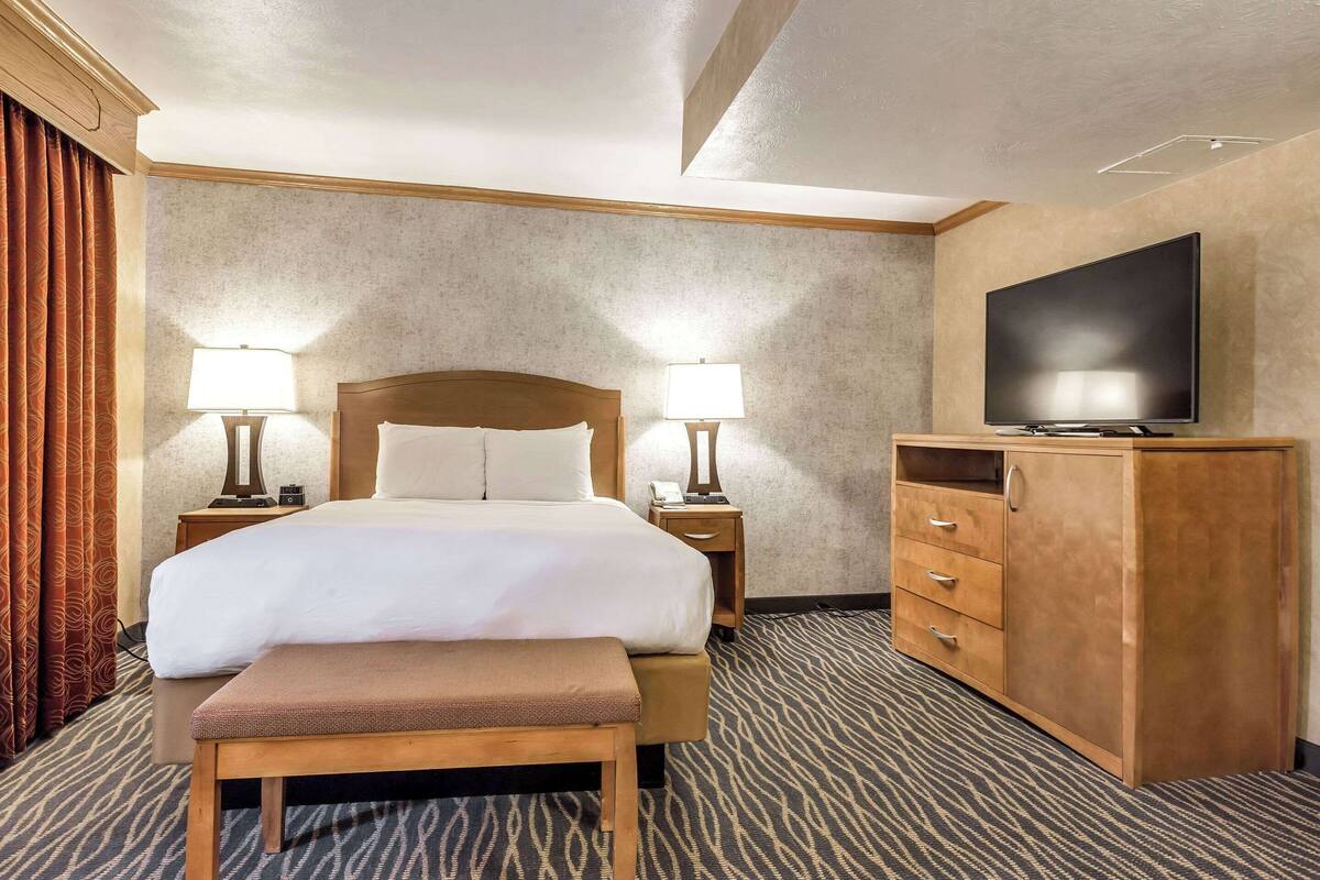 A hotel room with a bed, bedside lamps, a TV, a wooden cabinet, and a patterned carpet.