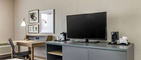 Habitación de hotel con cama, escritorio, silla, televisor y cafetera.