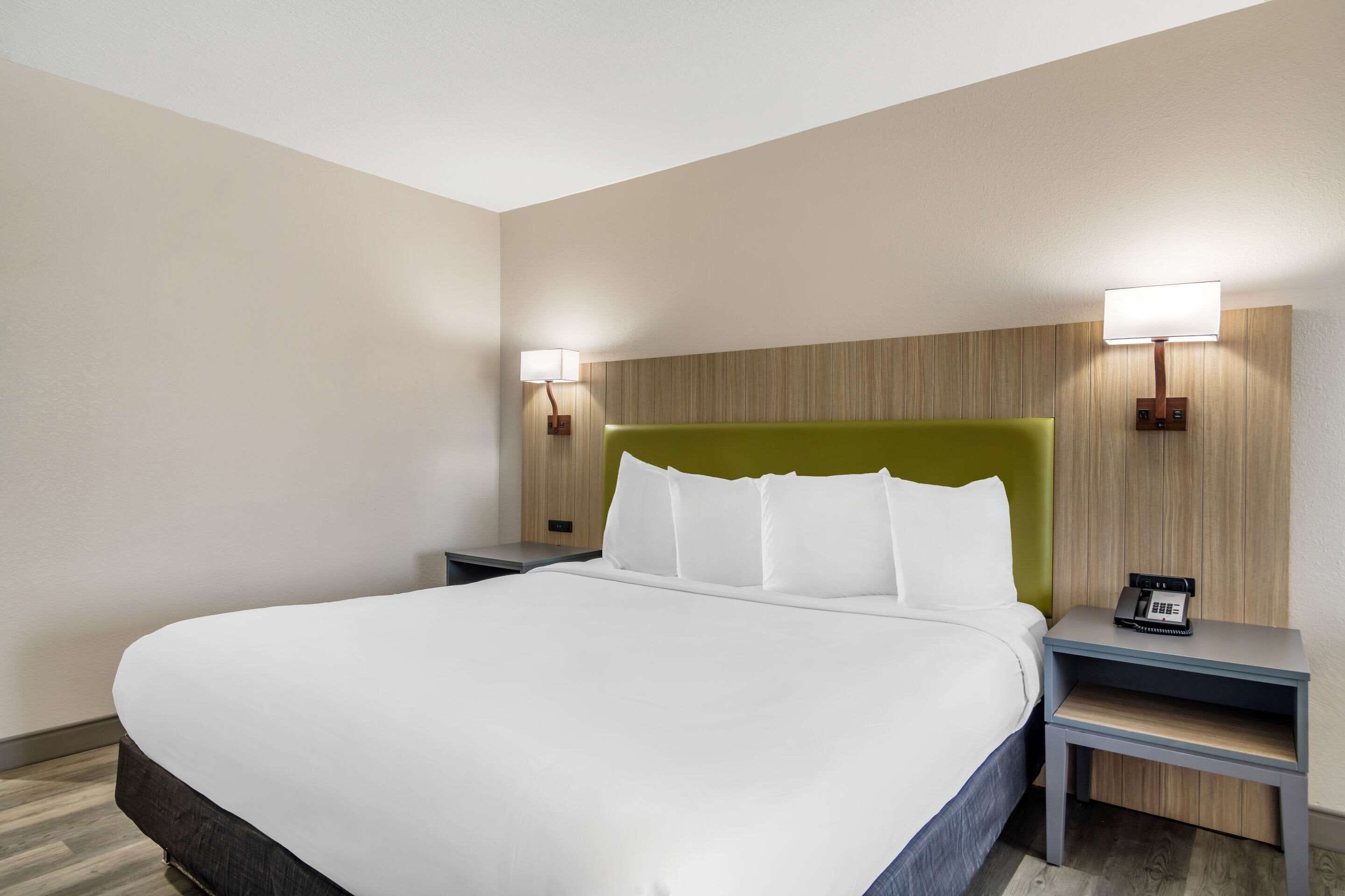 Una habitación de hotel con una cama grande, dos mesitas de noche con lámparas y un cabecero verde.