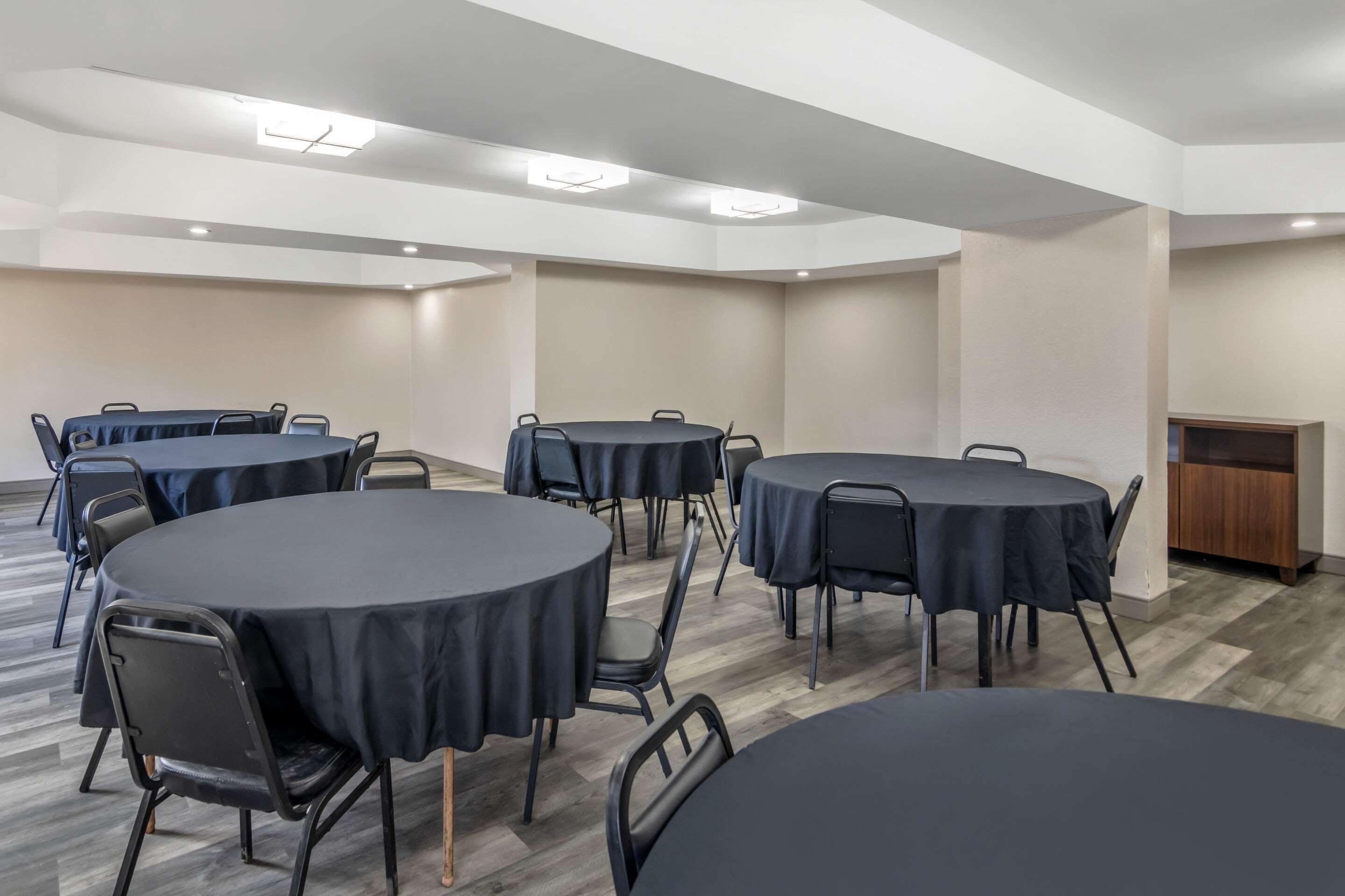 Un salón de conferencias con varias mesas redondas, sillas negras y un mueble de madera.
