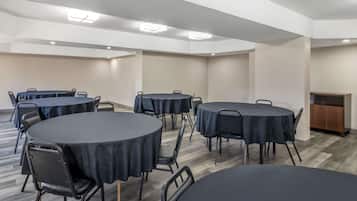 A conference room with multiple round tables, black chairs, and a wooden cabinet.