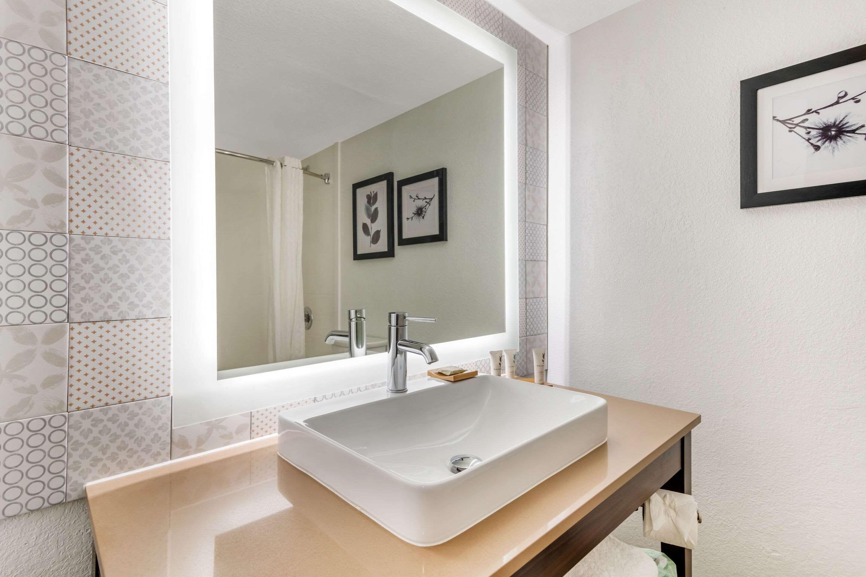 Une salle de bain moderne avec un grand miroir, un lavabo blanc et des carreaux à motifs.