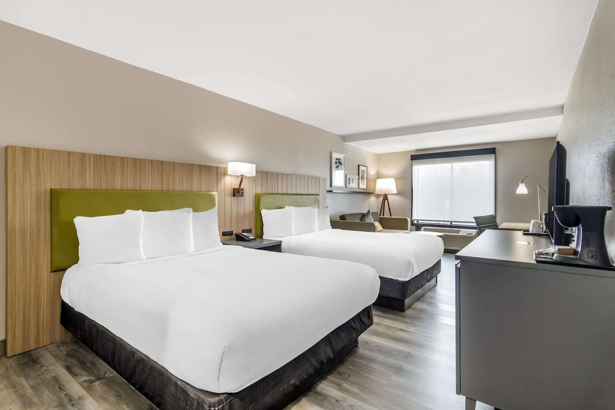 A hotel room with two beds, a desk, and a chair.