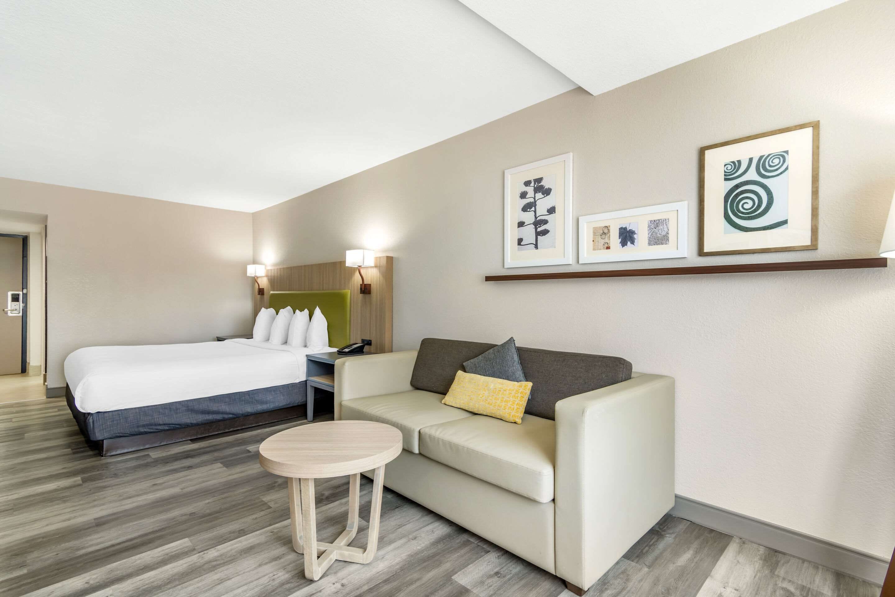 Quarto de hotel com cama, sofá, mesinha e obras de arte nas paredes.