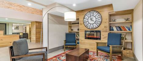 A modern living room with a large wall clock, two blue chairs, a wooden coffee table, and a patterned rug.