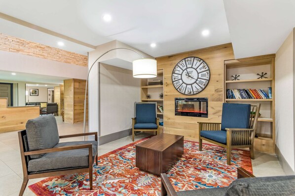 A modern living room with a large wall clock, two blue chairs, a wooden coffee table, and a patterned rug.
