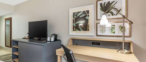 Habitación de hotel con escritorio, silla, televisor y cuadros en la pared.