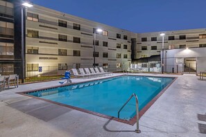 A swimming pool with lounge chairs and a modern building in the background.