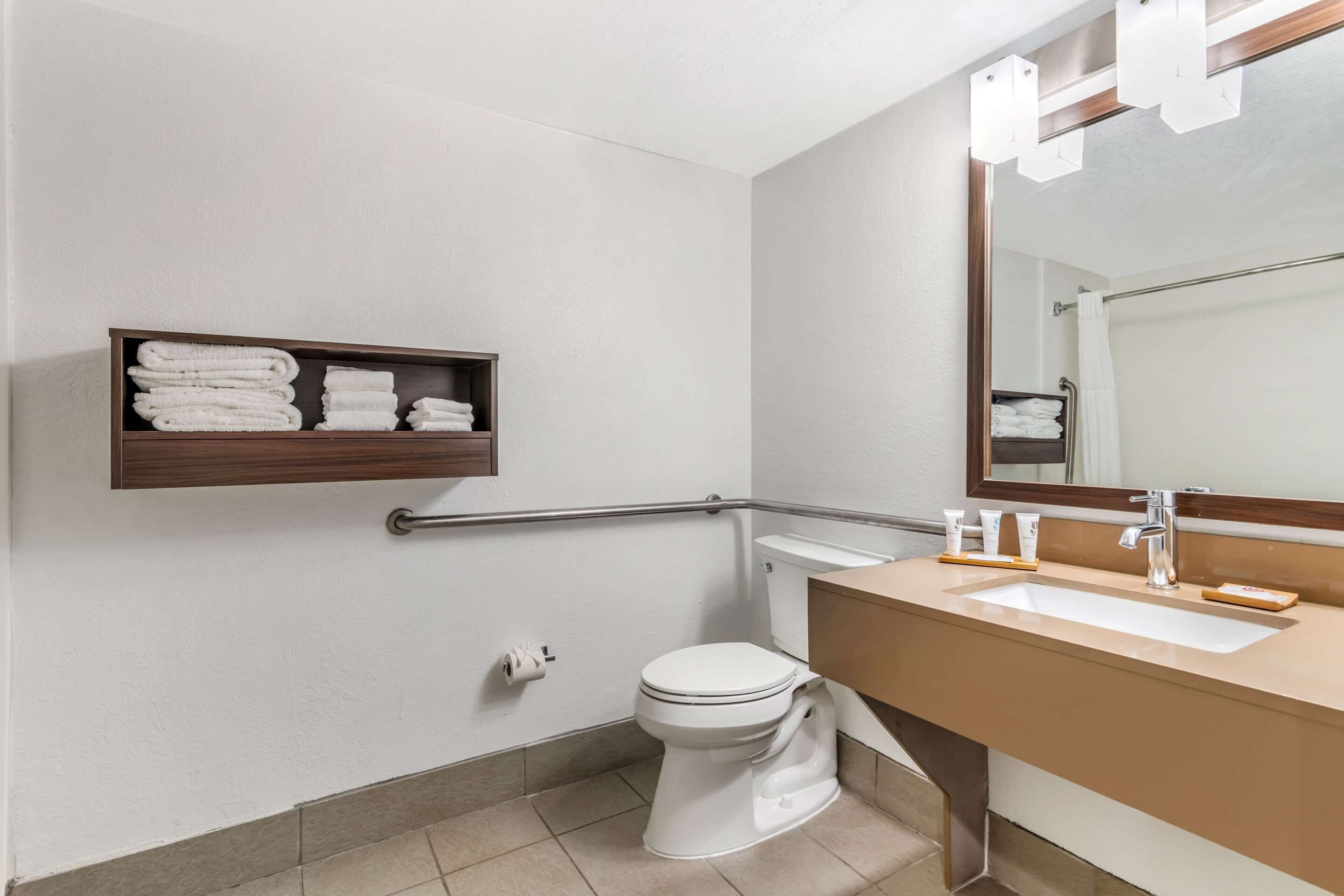 A bathroom with a white toilet, a beige sink, a mirror, and a shelf with folded towels.