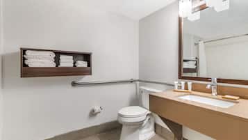 A bathroom with a white toilet, a beige sink, a mirror, and a shelf with folded towels.