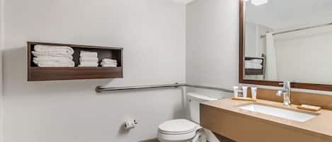 A bathroom with a white toilet, a beige sink, a mirror, and a shelf with folded towels.