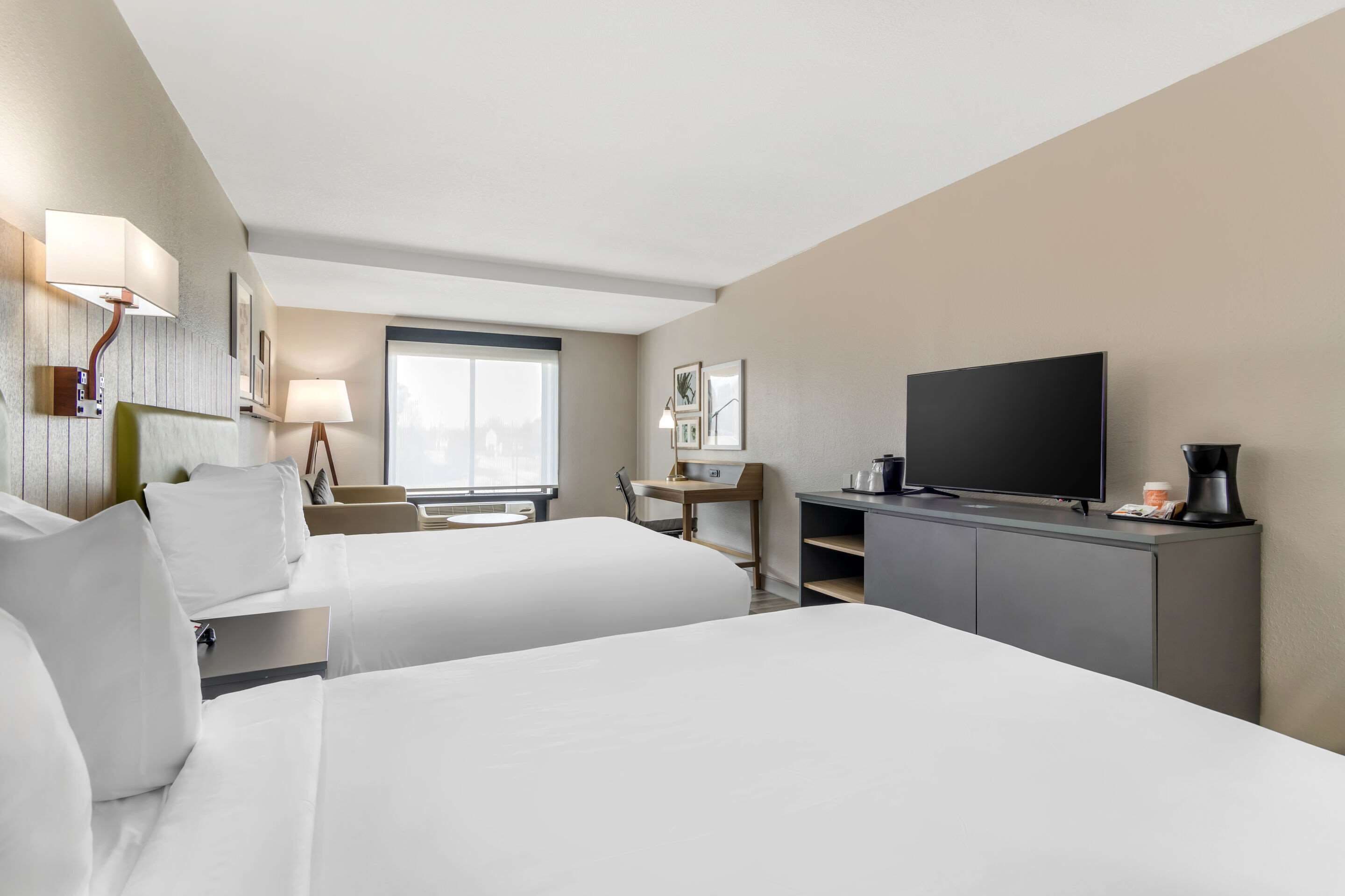 Een hotelkamer met twee bedden, een televisie, een bureau met een lamp en een raam.