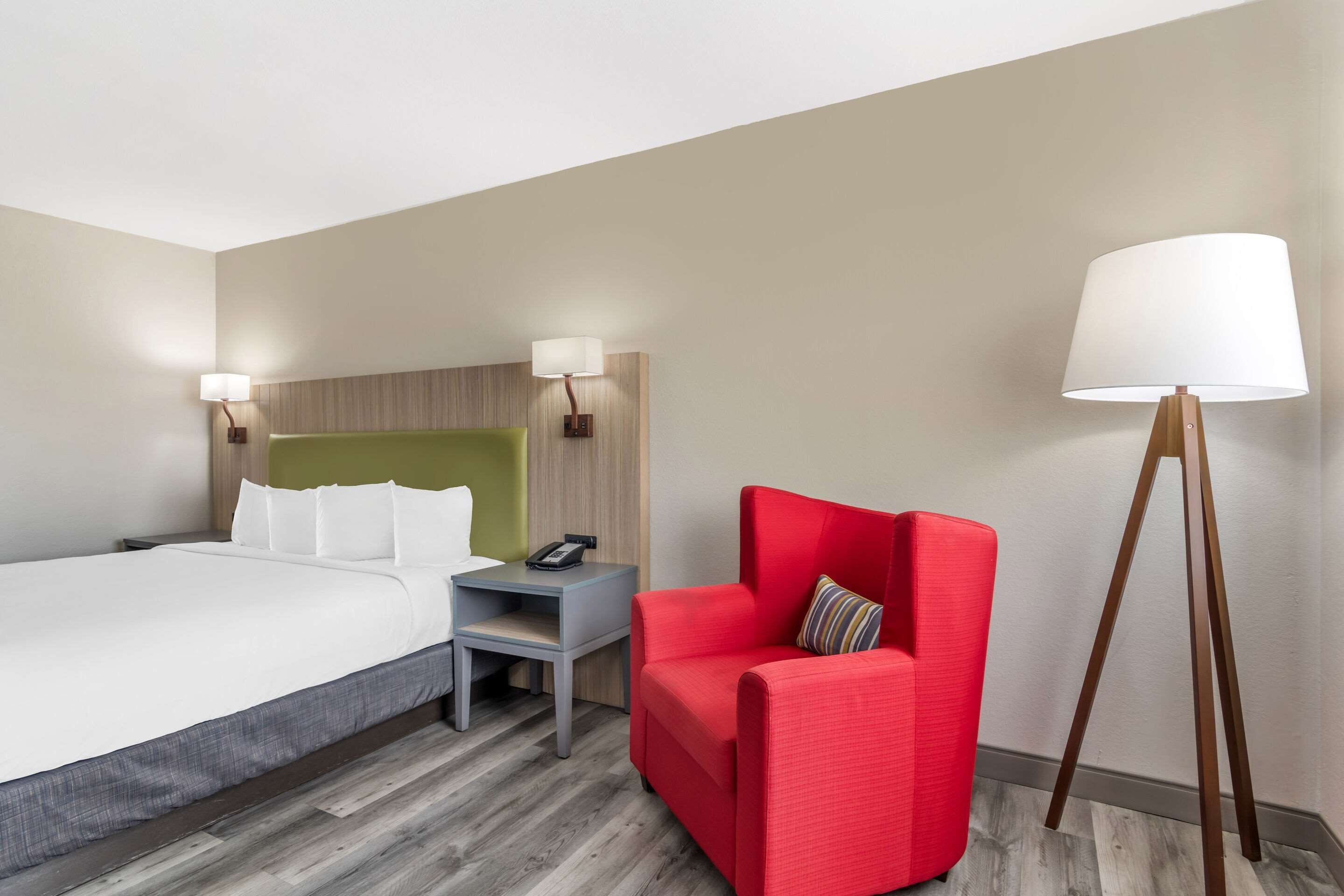 A hotel room with a bed, a nightstand, a red armchair, and a floor lamp.