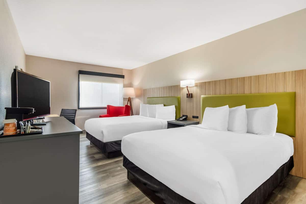 A hotel room with two beds, a desk, a TV, and a window.