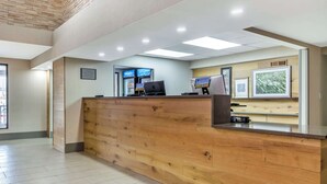 A reception area with a wooden reception desk, two computer monitors, and framed pictures on the wall. - Country Inn & Suites by Radisson, Atlanta Airport South, GA (College Park)