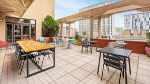 An outdoor patio area with tables and chairs, a wooden table, and a view of buildings in the background. - Ibis Styles Toulouse Centre Canal du Midi (Toulouse)