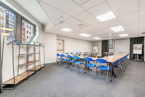 Una sala de conferencias con una larga mesa, sillas azules, una pantalla de proyector y una pizarra.