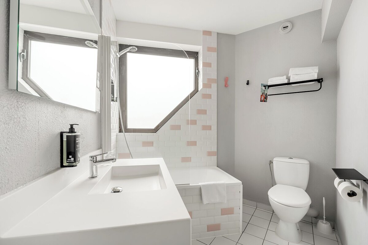 Un baño moderno con un ventanal grande, un lavamanos blanco, un inodoro y una ducha.